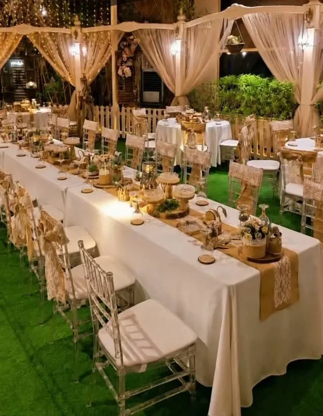 Long banquet tables in white linen with candles, under sheer drapes and string lights at Gardinya Park