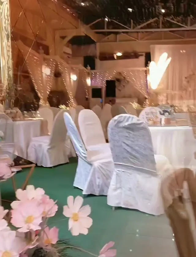 Covered event space with white chair covers, white tables and curtains of fairy lights